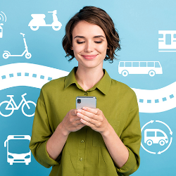 Man sieht eine junge Frau in einer grünen Bluse, die auf ihr Smartphone schaut. Auf der Wand hinter ihr sind verschiedene Fortbewegungsmitell, wie Bus, Fahrrad, Roller, Bahn etc. sowie eine Straße gezeichnet dargestellt.