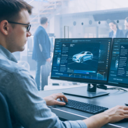 Ein Mann betrachtet in einem modernen, technischen Umfeld mehrere Bildschirme, auf denen 3D-Darstellungen und Daten eines Autos und dessen Antriebssystems angezeigt werden.