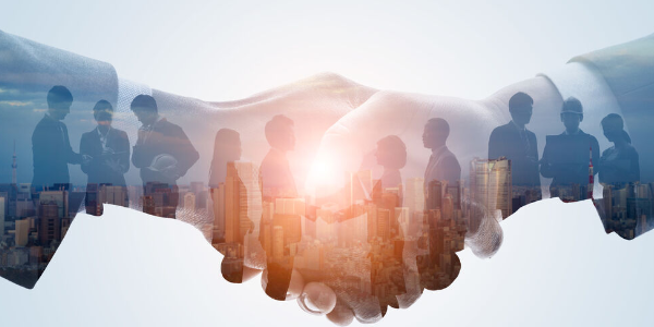 Das Bild zeigt zwei sich reichende Hände vor einer Stadtansicht, in die Silhouetten von Menschen in Geschäftsbesprechungen eingeblendet sind.