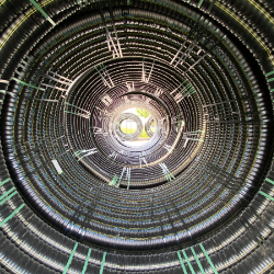 Das Bild zeigt die Innenansicht eines großen, spiralförmig gewickelten Rohrs mit Lichteinfall am Ende.